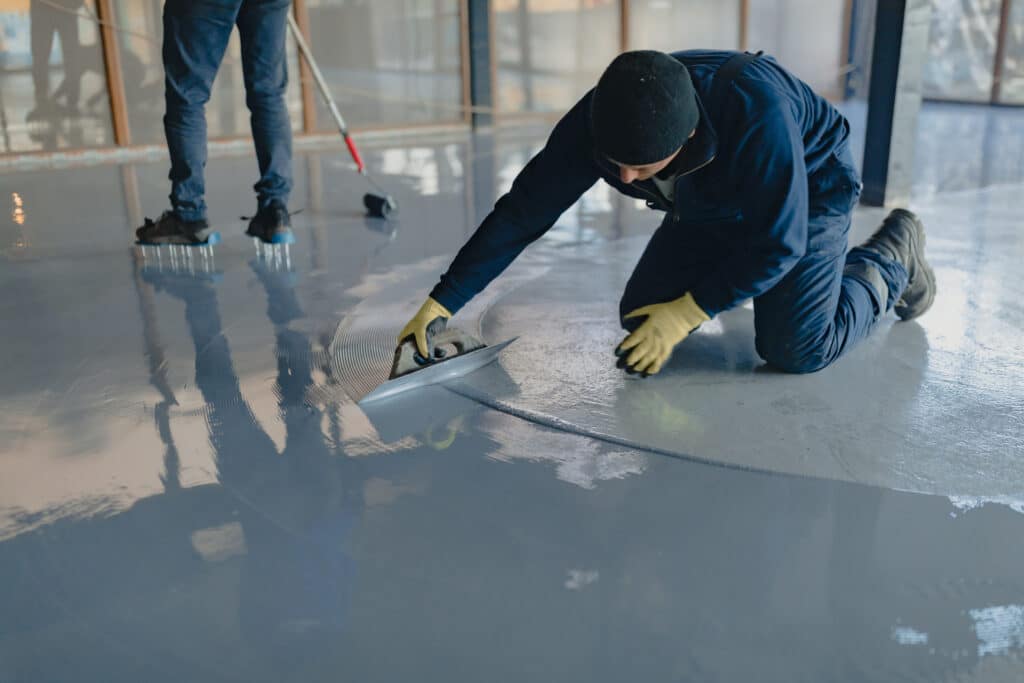 Is There a Better Time of Year to Install A Garage Floor Coating? The worker applies gray epoxy resin to the new floor. Install A Garage Floor